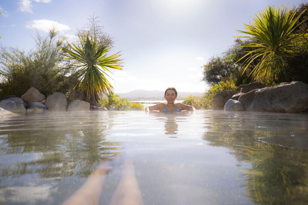 Une femme qui se baigne au Polynesian Spa, à Rotorua. Des montagnes et arbres exotiques en arrière plan. Source d'eau chaude de Nouvelle-Zélande