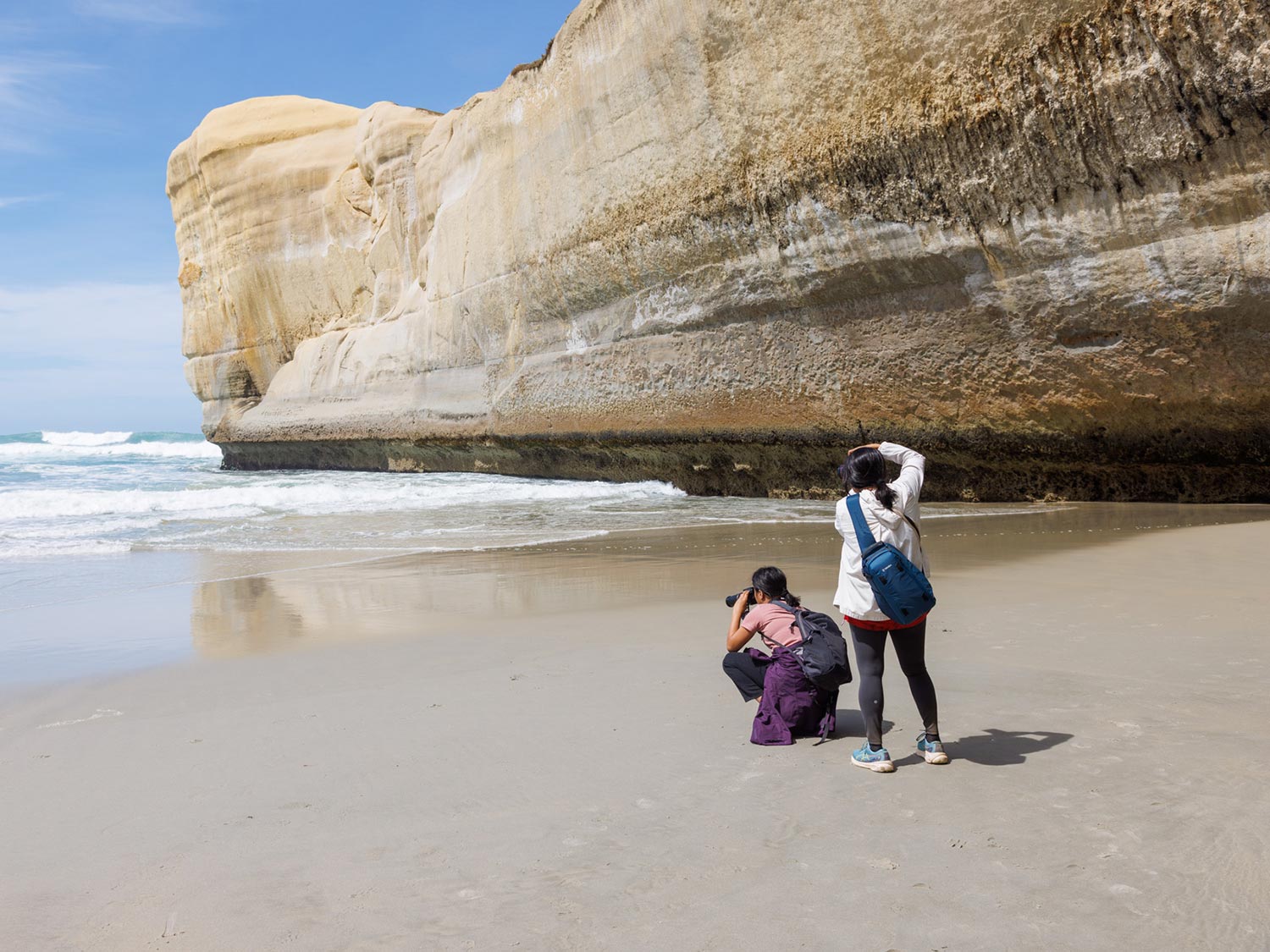 Deux personnes sur une plage photographiant la mer à Tunnel Beach en Nouvelle-Zélande