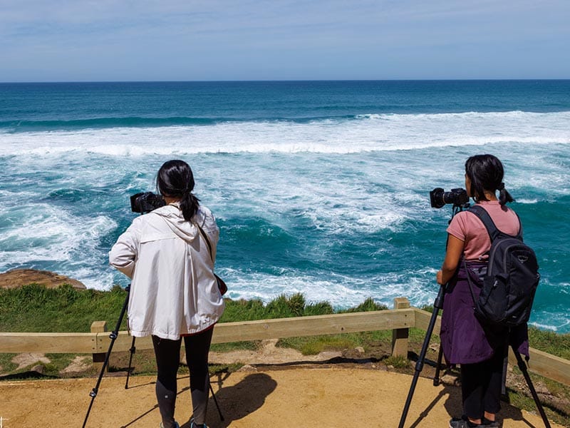 Deux personnes photographiant la mer à Tunnel Beach en Nouvelle-Zélande