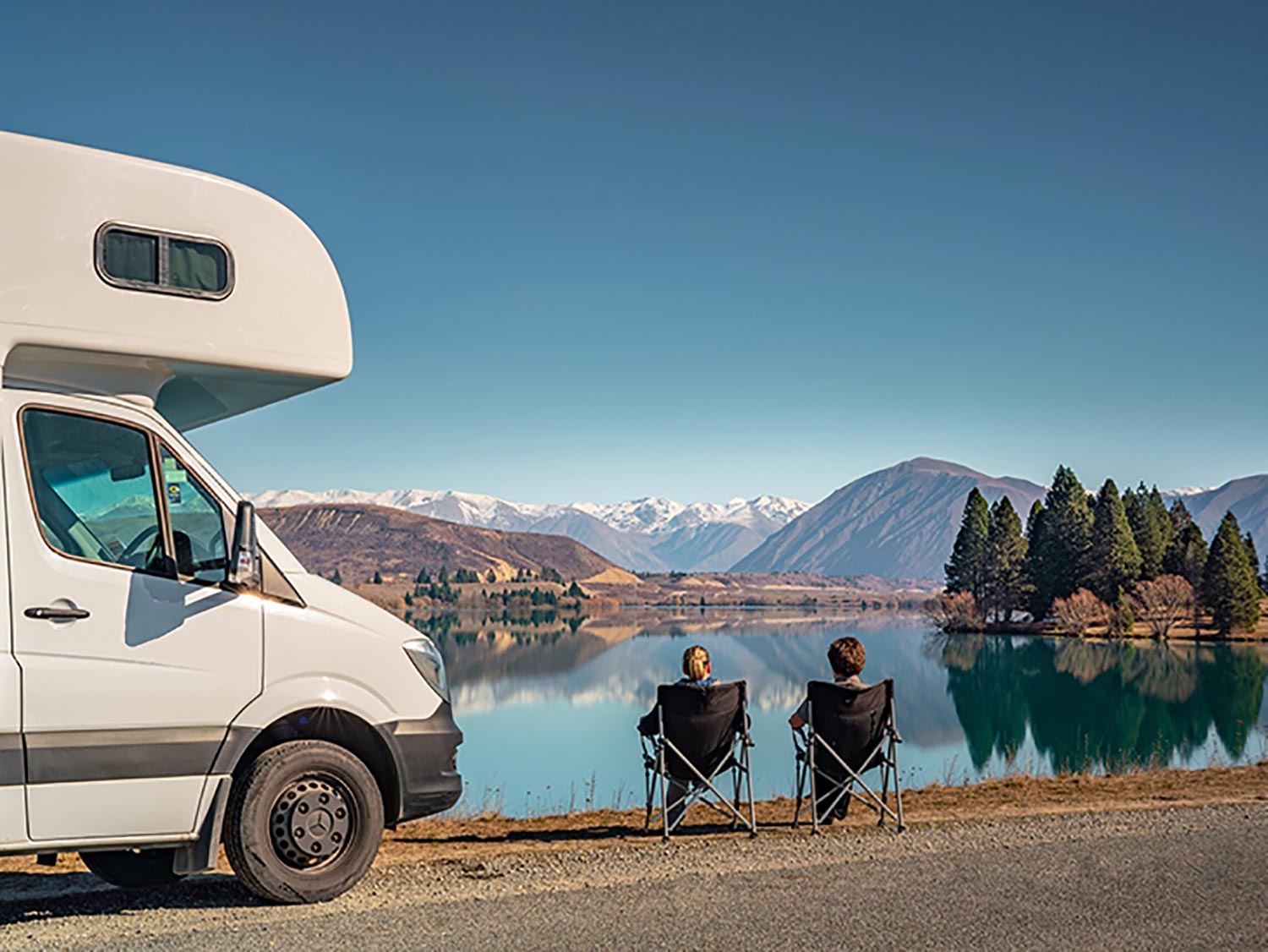 Deux vacanciers près de leur camping-car admirent un lac en Nouvelle-Zélande