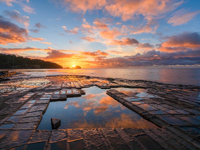 Coucher de soleil sur des rochers plats en forme de dalles en bord de mer en Tasmanie, Australie