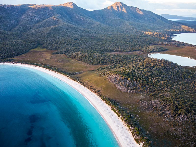 Vue aérienne d'une longue plage bordée de forêt et de montagnes dans le parc national de Freycinet en Tasmanie, Australie