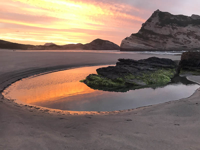 Un rocher entouré d'eau sur une plage au coucher du soleil en Nouvelle-Zélande